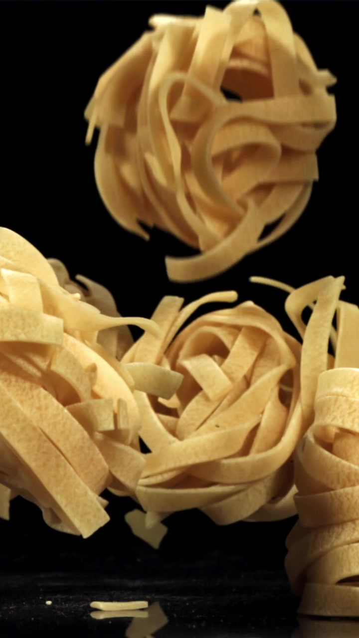 Nidi di fettuccine crude che cadono al rallentatore su sfondo nero