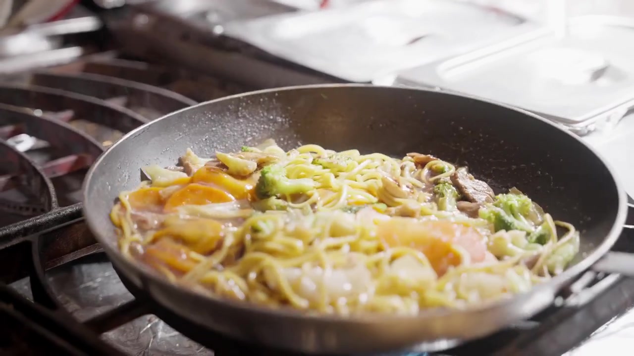コンロで調理中のフライパンでパスタにソースがかけられているクローズアップショット