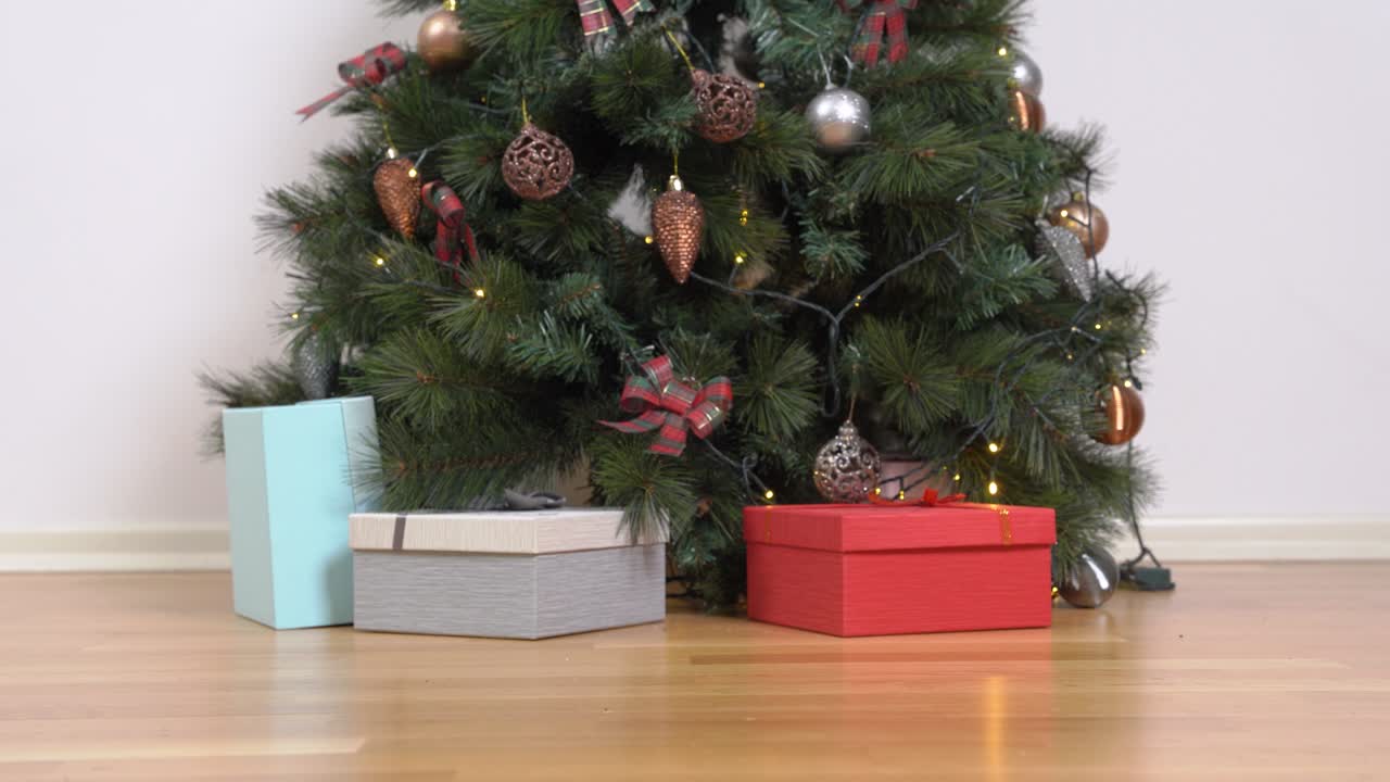 un cachorro de perrito juguetón con suéter y sombrero de santa claus mira las cajas de regalos cerca del árbol de navidad y huye a lo largo de la habitación.