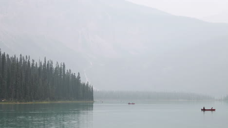 Toma-De-Teleobjetivo-De-Una-Canoa-En-Un-Lago-Con-Montañas-Humeantes-En-El-Fondo-En-4k