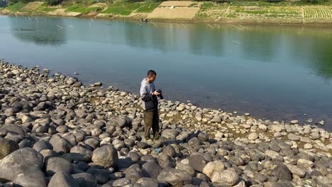 Traveler-young-Asian-man-takes-a-photo-with-a-film-camera-in-the-forest-mountain-river-lake-at-sunset,-Happy-to-travel-nature-outdoors