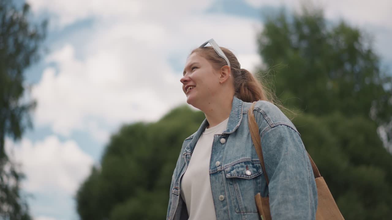 Sguardo giovanile verso il cielo. Donna sorridente che osserva le nuvole all'aperto. Donna dai capelli chiari che osserva pensierosa il cielo coperto. Giovane donna allegra vestita in denim guarda serenamente il cielo estivo nuvoloso.