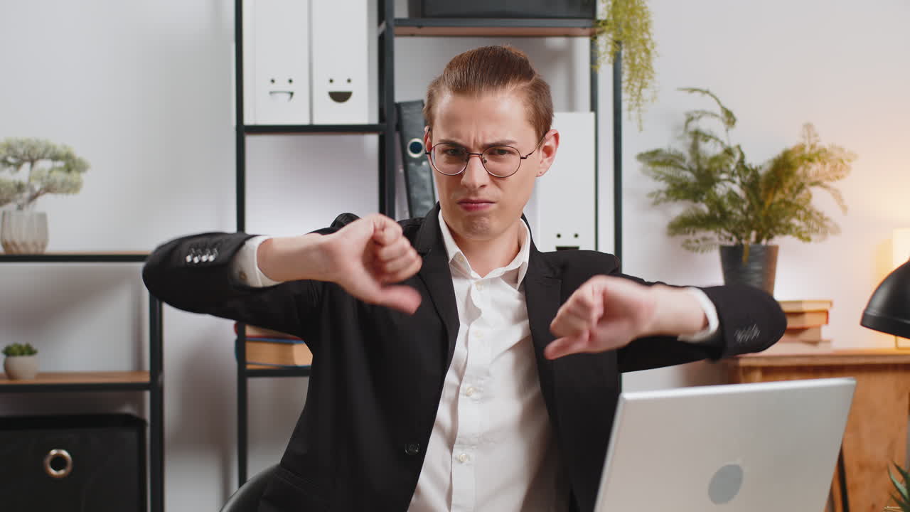 Upset young caucasian businessman freelancer showing double thumbs down sitting at home office desk