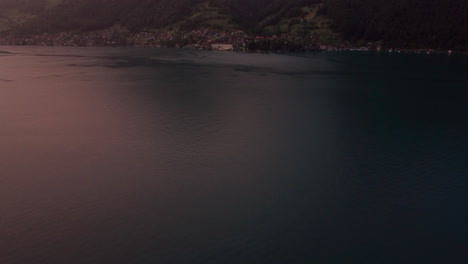 aerial-tilting-up-revealing-the-picturesque-mountain-town-of-Merligen-at-the-feet-of-towering-mountain-on-the-shore-of-lake-Thun