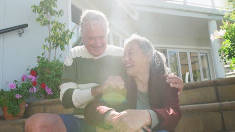 happy diverse senior couple sitting on stairs on sunny day in garden