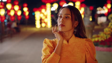 Woman-in-yellow-Ao-Dai-touching-her-hair,-vibrant-Hoi-An-lanterns-at-night