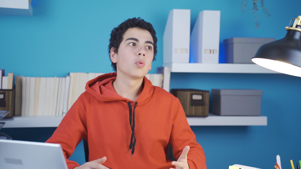 un joven adolescente que mira una computadora portátil se sorprende por lo que ve en la pantalla y mira a su alrededor sorprendido.