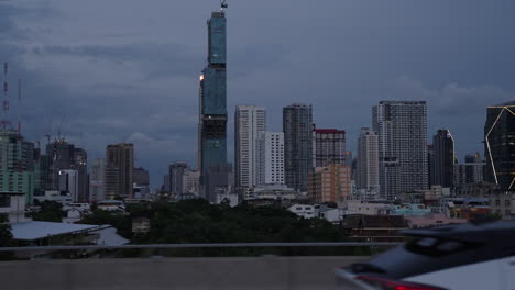 driving along bangkok elevated expressway during blue hour, view of bangkok city skyline and high raised construction sites