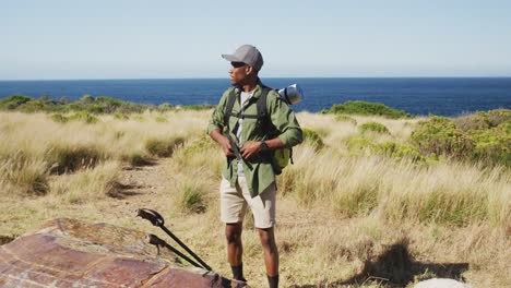 hombre afroamericano haciendo senderismo en el campo por la costa tomando un descanso