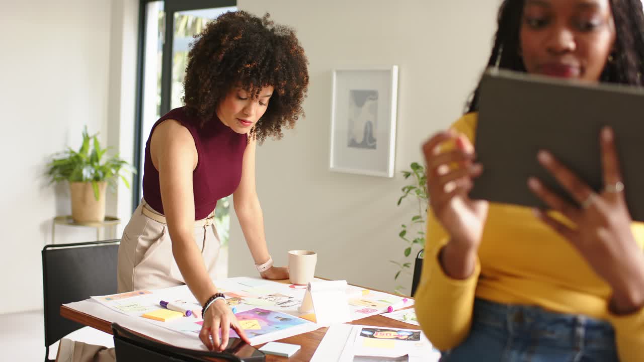 Scrolling smartphone, Diverse female coworkers arranging design mockups swiping tablet in office