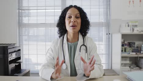 biracial female doctor sitting at desk and having video call, slow motion
