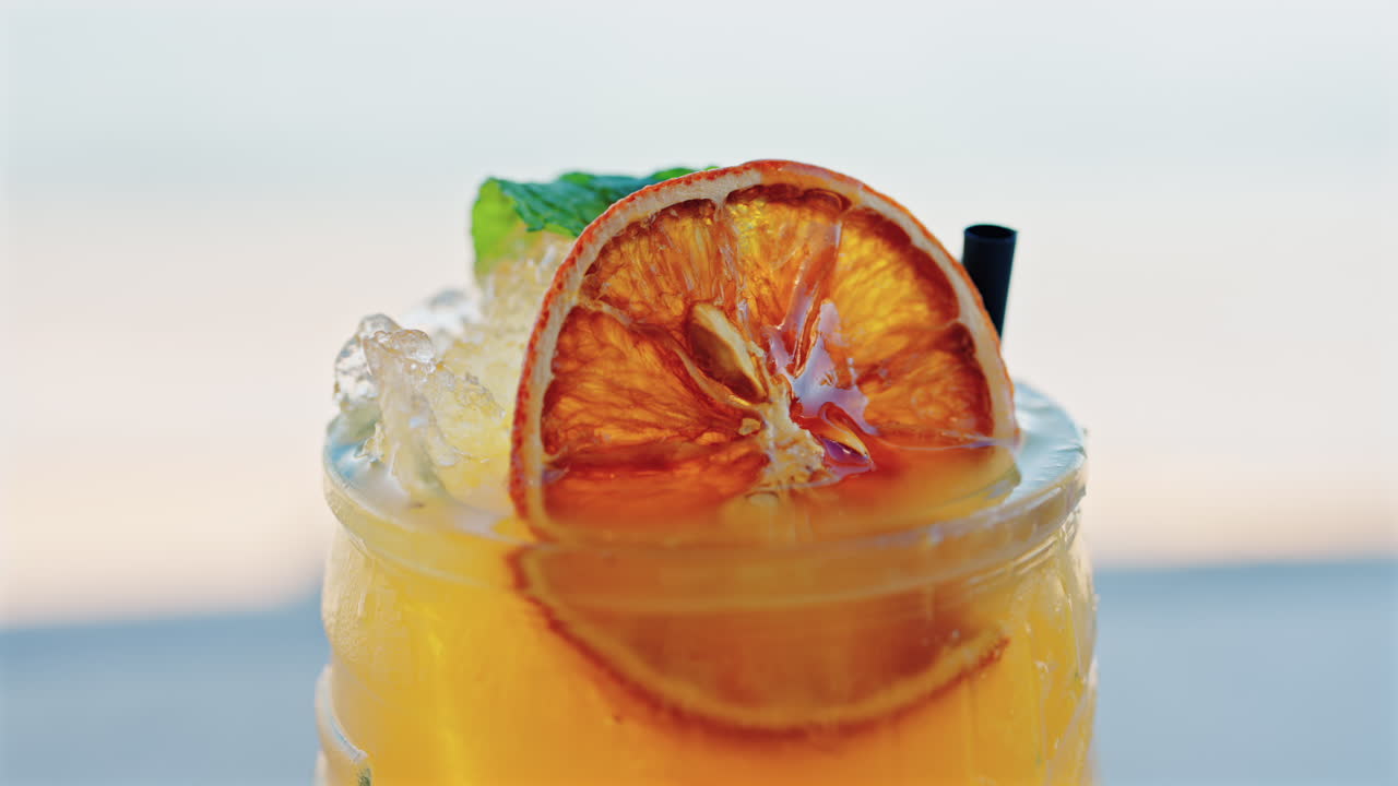 Close up of an orange cocktail on a table with a blurred view of the sea on the background