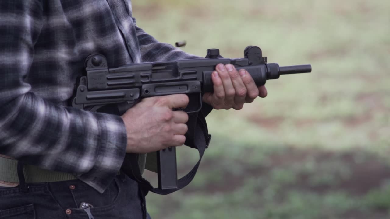 Medium shot of a man testing a small submachine gun. Close up