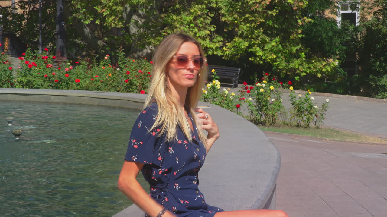 금발 우크라이나 여자 모델 휴대 전화 분수 가장자리에 앉아 selfie 걸립니다