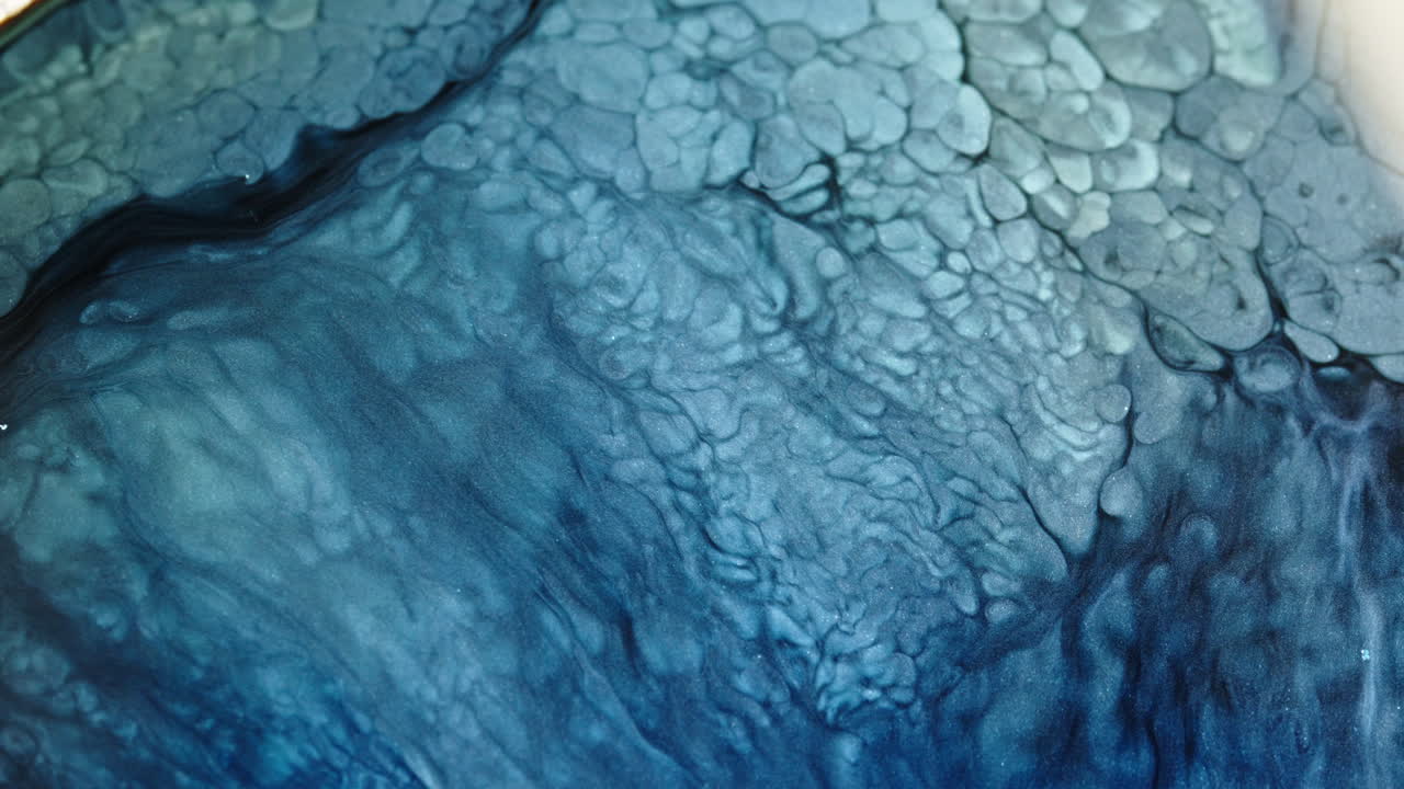 Vibrant blue liquid patterns swirl and mix in intricate macro detail, creating a dynamic abstract effect