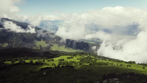 aerial drone shot of a grass covered mountain top with a small trail leading up with clouds around