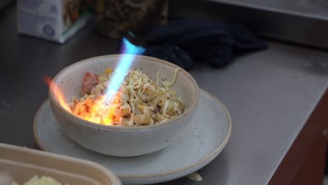 Movimiento-De-Mano-Toma-De-Primer-Plano-De-Chef-Profesional-Antorcha-Un-Tazón-Deliciosos-Y-Sabrosos-Macarrones-Con-Queso,-Adultos-Y-Niños-Comida-Reconfortante-Favorita