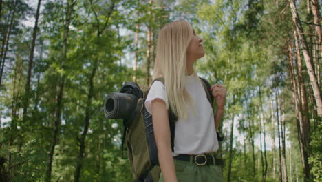 una mujer camina por el bosque en un soleado día de verano en pantalones cortos y una camiseta sonriendo y examinando la belleza de la naturaleza y el bosque