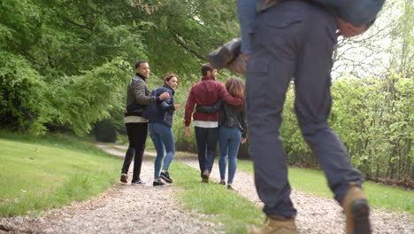 young couples walk and piggyback in country lane, back view