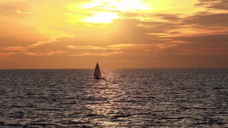 slow motion sailboat sails through sunset in calm waters