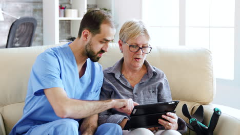 Male-assistant-teaching-senior-retired-elderly-old-woman-how-to-use-her-tablet-computer