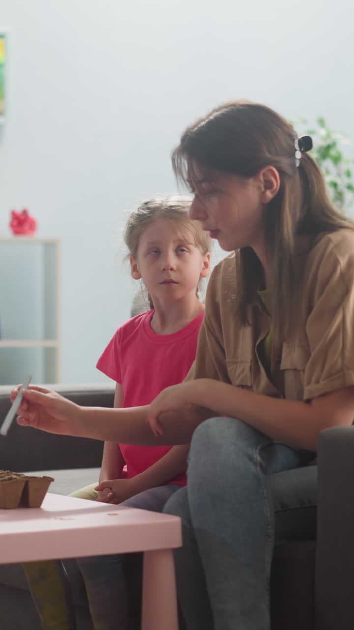 a young woman with little children in the room is planting plants, a mother shows two children a boy and a girl how to make holes for seeds in peat pots