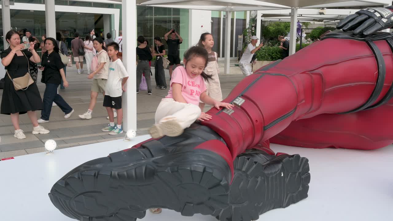 Children climb an 8-meter Marvel Deadpool installation as locals and tourists take photos. The display promotes Disney's movie "Deadpool and Wolverine" in Hong Kong.