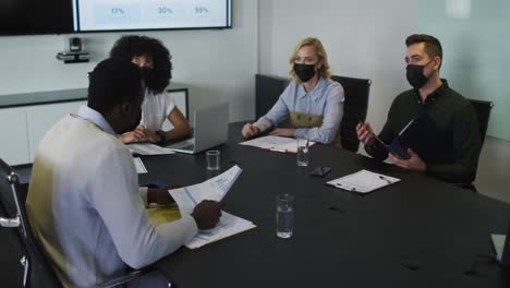 diverse group of business colleagues wearing masks in discussion in meeting room