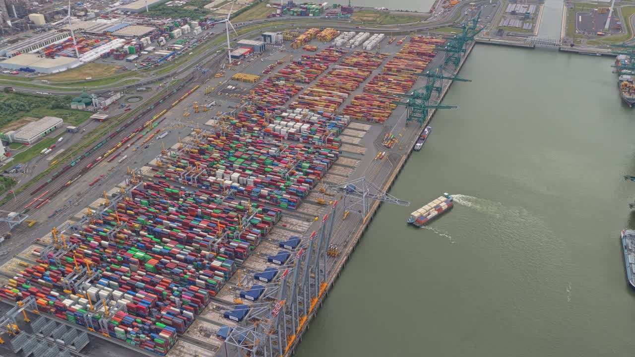 Aerial drone over busy industrial port with container ship and cranes, Belgium