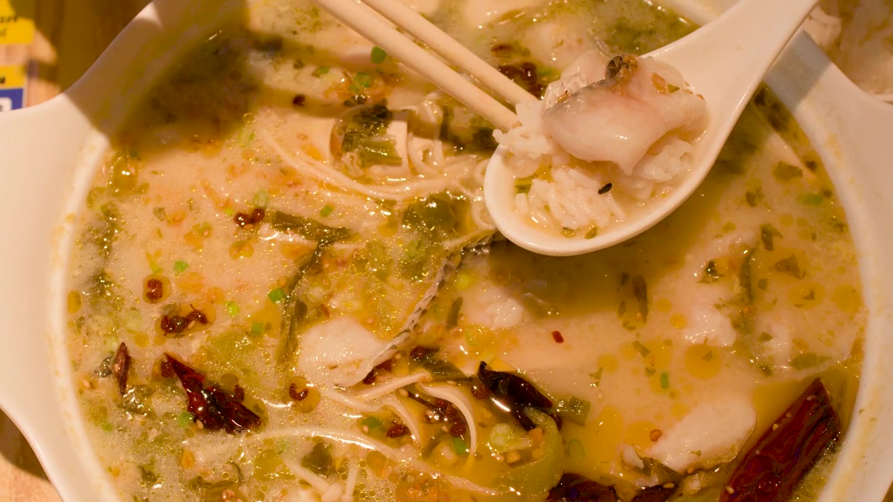 Ovenfra-skud af en person, der bruger spisepinde og ske til at spise krydret fiskesuppe med ris.