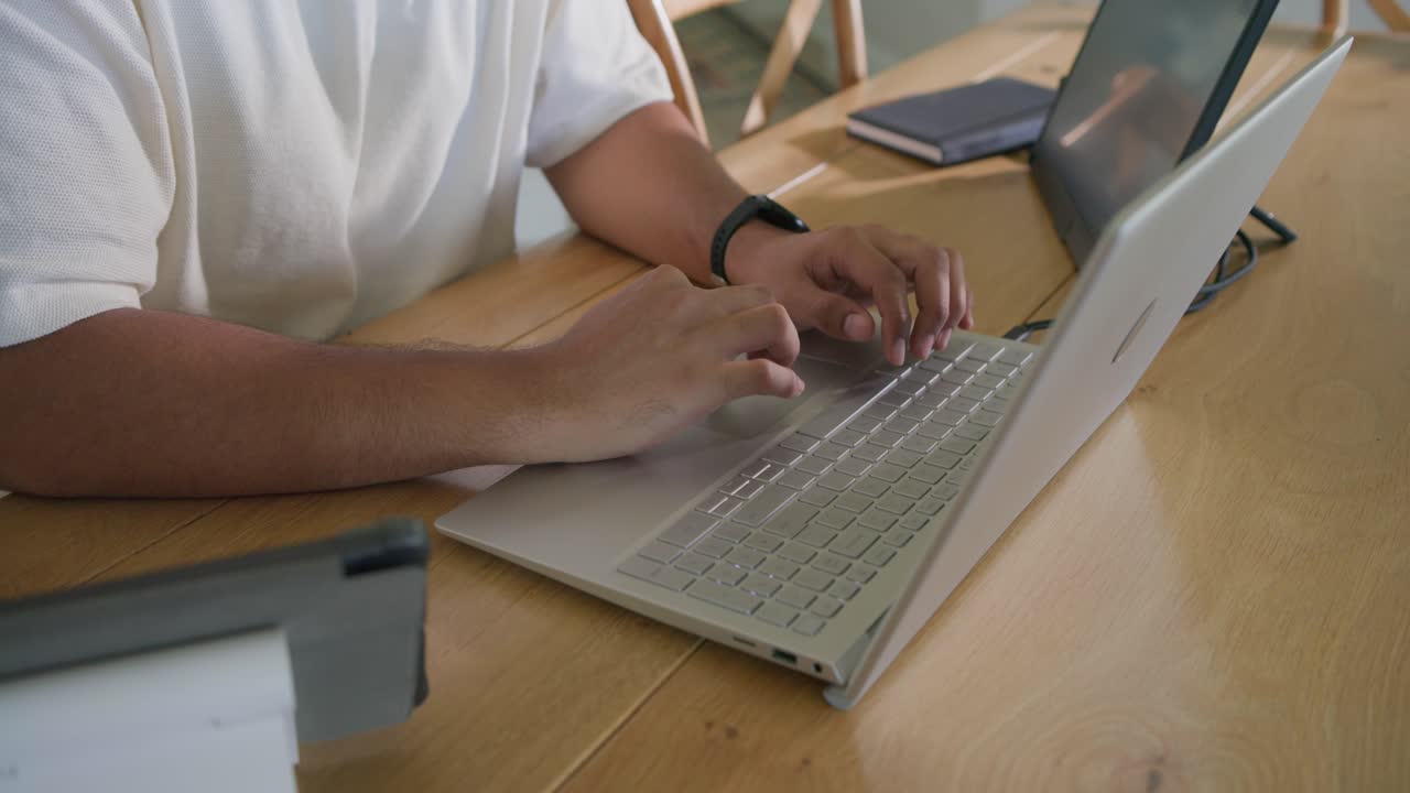 Hands landing on keyboard, mid adult African American man typing on silver laptop completing work
