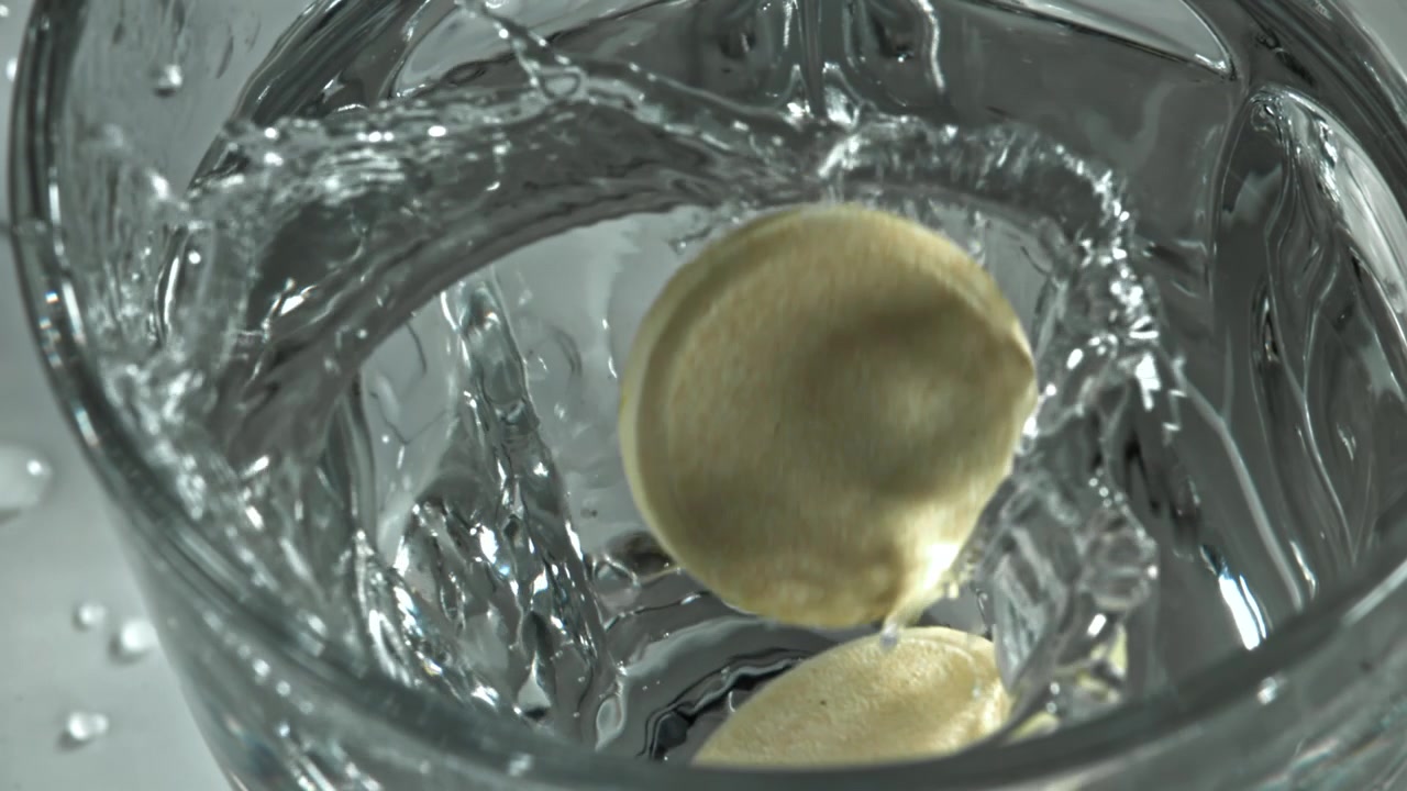 Brausetablette fällt in Zeitlupe in ein Glas Wasser