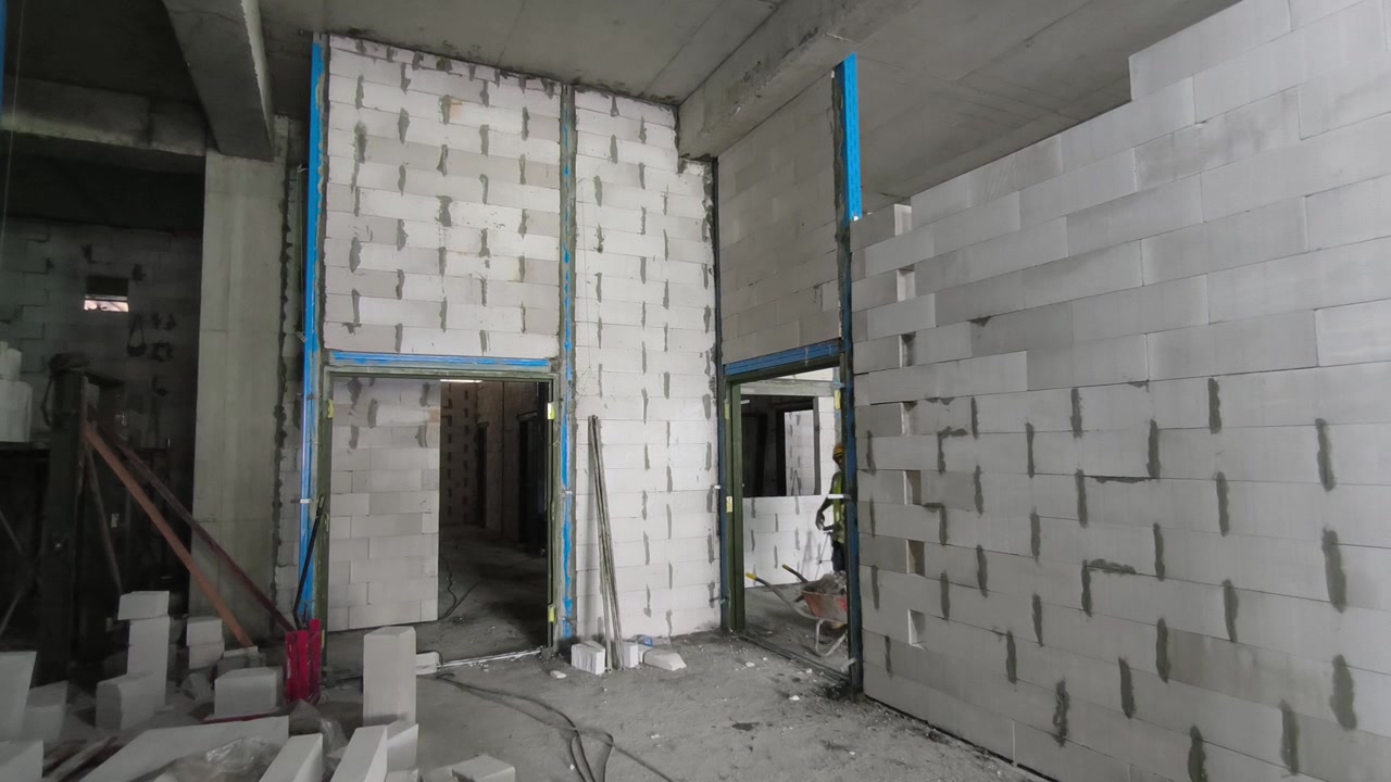 Instalación de muro de bloques de hormigón celular autoclavado (HCA) en una obra de construcción. Incorpora refuerzos metálicos y dinteles para eficiencia estructural. Las técnicas modernas de mampostería aceleran el progreso de la construcción
