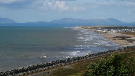 looking across a railway line through to coastal waves and beach and in the background can be seen the mountains of the llyn peninsula, wales, uk - 10 second version