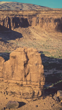 a lone rock formation stands tall in a vast canyon, the sun casting long shadows across the desert landscape.