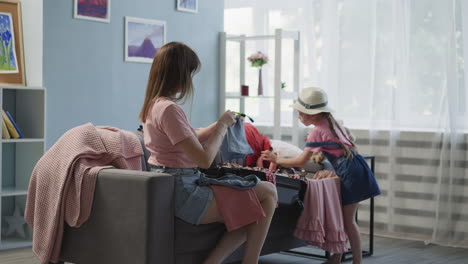 mother gathers apparel daughter puts toys into suitcase