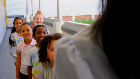 schoolkids with teacher standing in row in hallway at school 4k