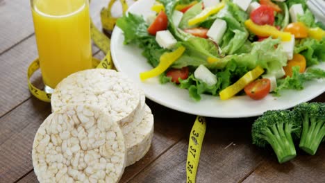 Vegetable-salad-with-glass-of-juice,-granola-bar-and-measurement-tape