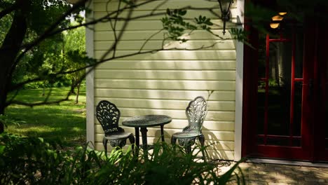 static-shot-showing-a-small-table-with-chairs-outside-of-a-building-with-leaves-and-tree-branches-blowing-in-the-wind-around-it