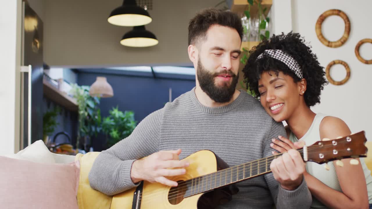 Video di una coppia felice e mista che si rilassa in soggiorno, l'uomo suona la chitarra e canta alla donna.