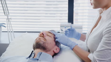 esteticista mujer dando a un paciente masculino maduro una inyección de botox en la frente