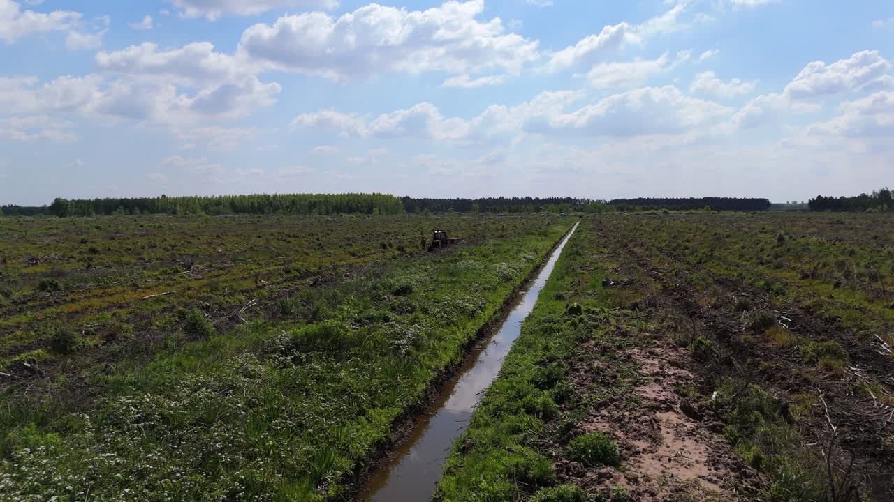 Irrigation canal flowing through cultivated fields under blue sky with clouds with workers tending to crops in the background, all under a bright blue sky, drone fpv shot