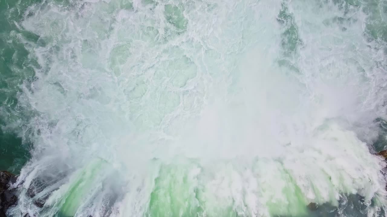 Static top down aerial shot of wide waterfall gushing into river in Iceland