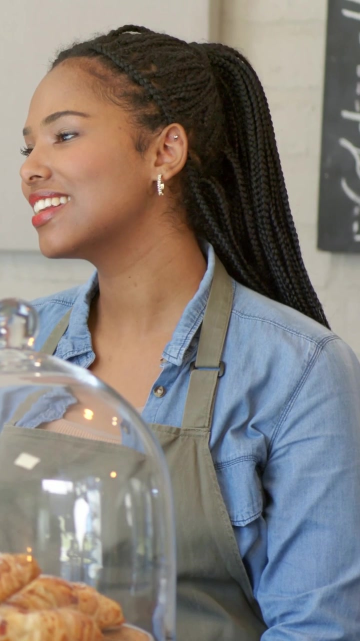 Vertical video: Responding barista in apron at cafe to customer asking, croissants under glass dome