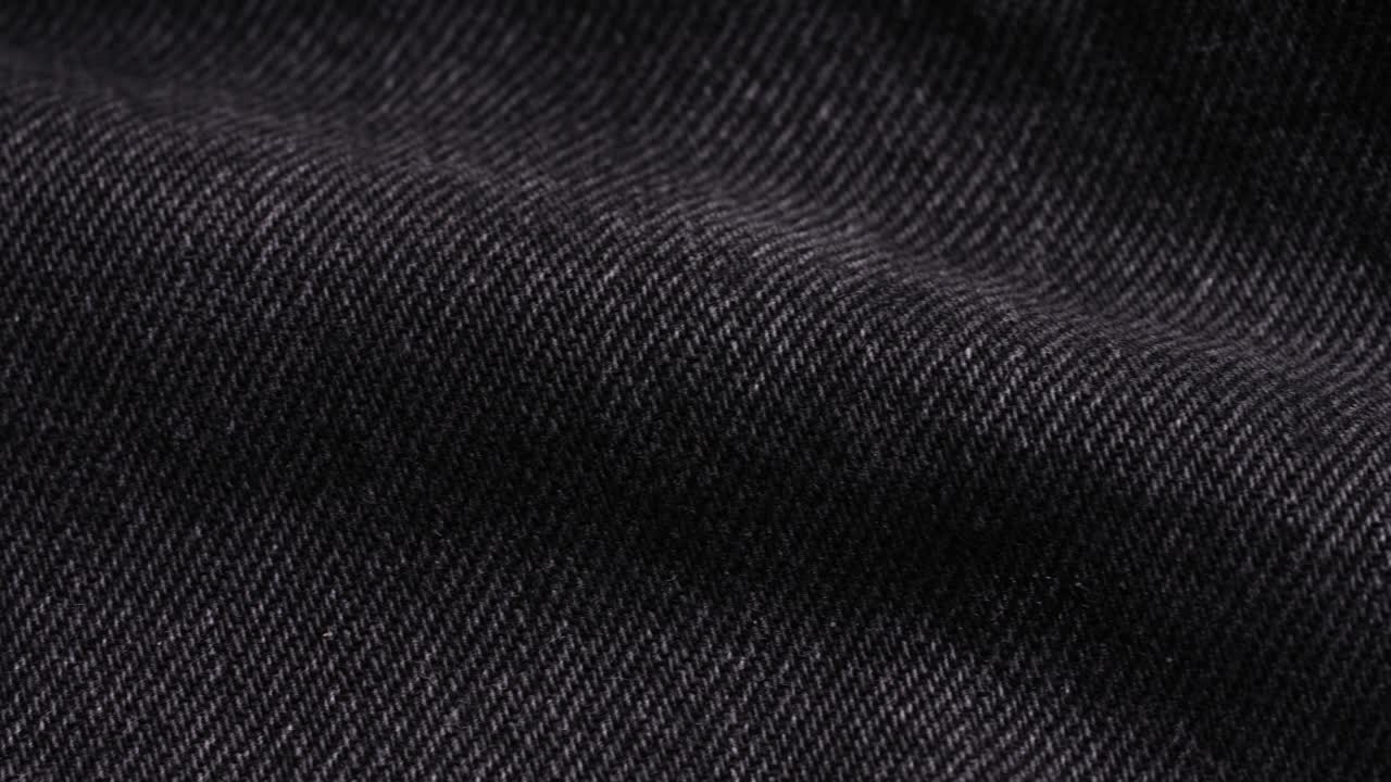 A black denim vest reveals twill texture and seam detail as the camera pans slowly from left to right