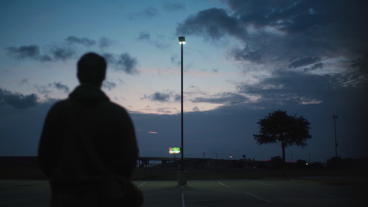 An onlooker watches a distant highway in a quiet parking lot