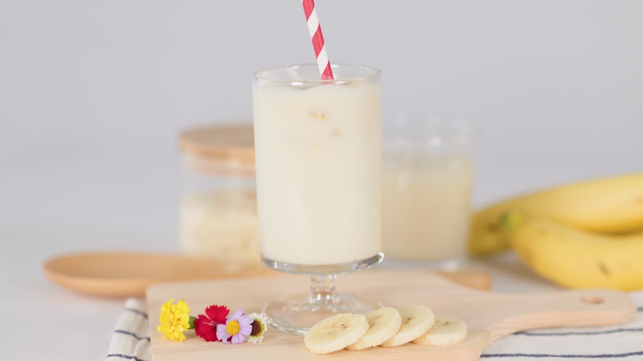 Frullato di latte e banana in un bicchiere con cannuccia su tagliere, primo piano statico