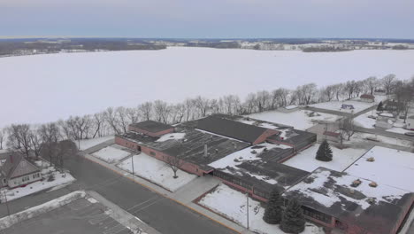 drone aerial shot over a frozen lake and small midwest town in the winter to a school