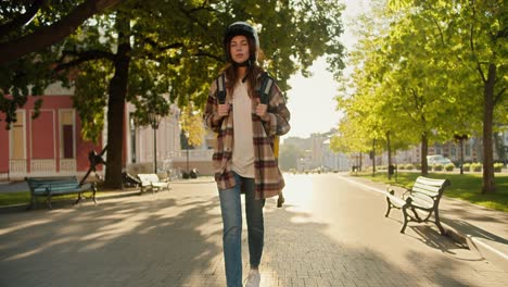 a brunette girl in a checkered shirt and denim pants with a white motorcycle helmet approaches her victory, sits on it and goes to work as a courier