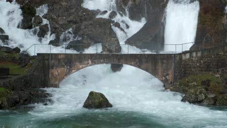 hillside gushing waterfalls flowing under arched bridge